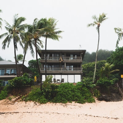 A two story beach-front property flanked by palm trees